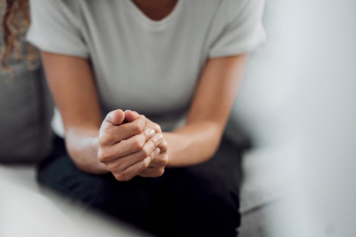 A woman sitting forward on a couch clasping her hands.