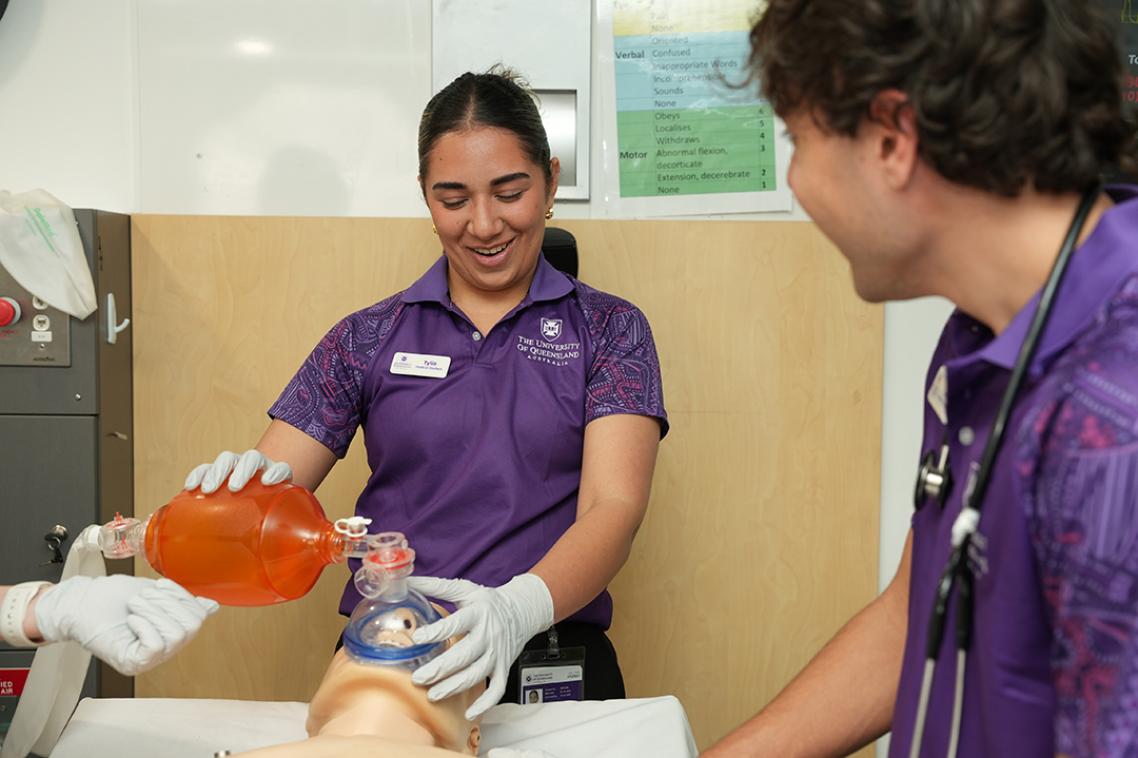 Two UQ students standing over a medical dummy.